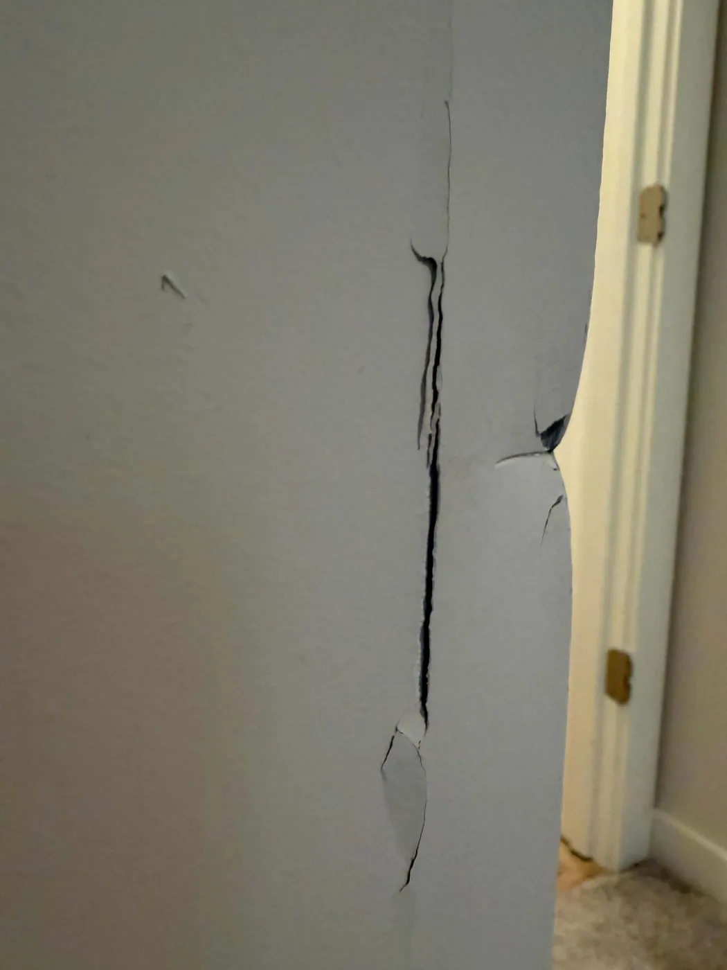 Large vertical crack and damaged drywall near a doorway