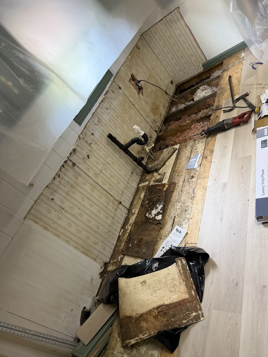 Kitchen floor exposed during early demolition, showing damaged subfloor and plumbing
