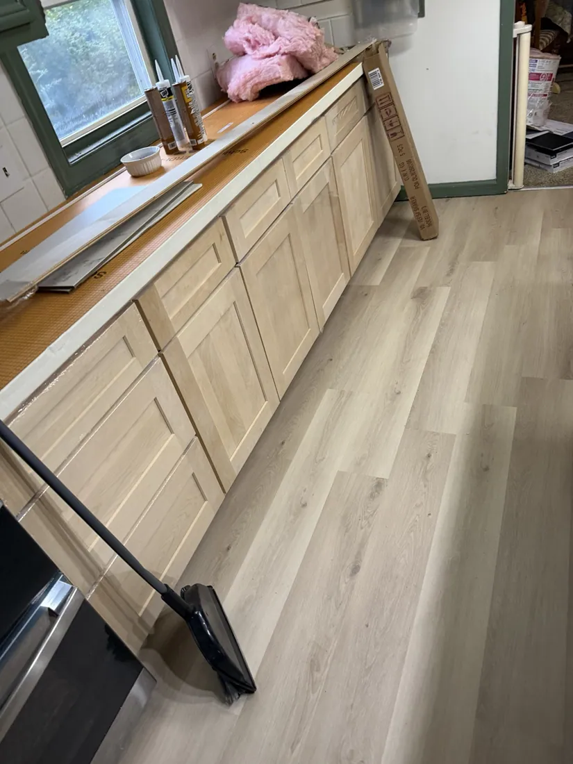 New light wood look kitchen flooring installed next to unfinished cabinetry